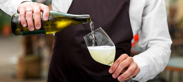 Barman pouring sparkling wine to the glass on the dark apron background